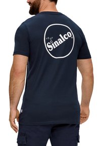 Granatowa bawełniana koszulka z krótkim rękawem z okrągłym białym logo z napisem "Sinalco" na plecach. Okrągły dekolt, gładka faktura.