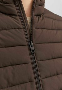 Brun isolerad väst med en kviltad mönstring, som har en dragkedja fram och en ståkrage för extra värme och stil.