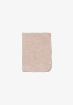 Serviette beige douce pliée avec bords arrondis et petite étiquette en tissu sur un coin contre un fond blanc.