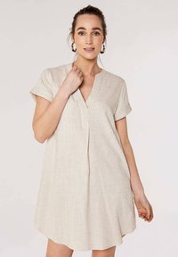 Robe en lin beige avec un col en V, des manches courtes et une coupe décontractée. Présente une texture douce et un ourlet légèrement incurvé pour un look casual.