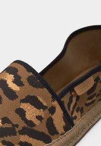 Κοντινό πλάνο παπουτσιού εσπαντρίγιας με λεοπάρ σχέδιο, μαύρο τελείωμα και πλεκτή σόλα από τζουτ, με μια μικρή ταμπέλα μάρκας σε ταμπά χρώμα στο εσωτερικό.