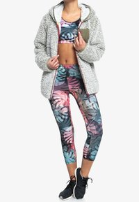 Grå fuzzy zip-up jakke med hætte, parret med farverig blomster sportstop og tights. Sorte træningssko fuldender outfittet.