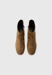 Brune mokkasiner ankelsko med en glatt tekstur, en tettsittende design og glidelåser på siden. Runde tær og minimale sømdetaljer.