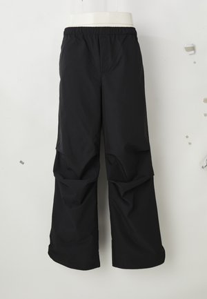 Black loose-fit pants with an elastic waistband, displayed hanging against a plain light background.