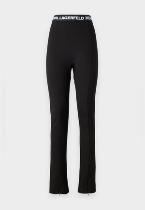 Čierne elastické nohavice so širokým pásom, na ktorom je biele písmeno "KARL LAGERFELD JEANS". Úzke prevedenie a zipsové detaily na leme.