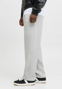 Pantaloni de trening gri, confecționați dintr-un material moale, cu un design cu picior drept și un detaliu de buzunar, asortați cu adidași negri.