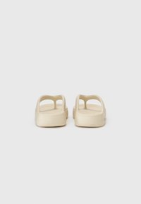 Beige sandaalit, joissa on avonaiset takapuolet, teksturoitu pohja ja kaksi sivureikää ilmanvaihtoa ja mukavuutta varten. Sujuva muovimateriaali.