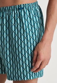 Patronen zwemshorts met een teal en witte geometrische print. Gemaakt van lichtgewicht stof, met een elastische tailleband voor comfort.