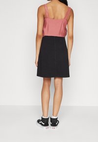 Woman wearing a pink sleeveless top with lace straps, a black knee-length skirt, and black high-top sneakers with white soles.