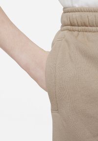 Béžové tepláky s texturovanou tkaninou, elastickým pasem a boční kapsou, představující ležérní design vhodný pro každodenní nošení.