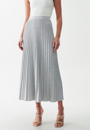 Light gray pleated skirt with a high waistband, made from textured fabric, falling to mid-calf, paired with light-colored strappy sandals.
