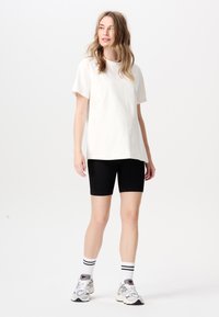 Witte katoenen t-shirt gecombineerd met zwarte geribbelde fietsshorts. Model draagt grijze sneakers met accenten en gestreepte witte sneakersokken.