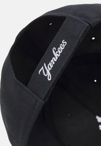 Gorra de béisbol azul marino hecha de tela texturizada con un logo blanco de "Yankees" bordado en la banda interior.