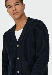 Marineblaue gerippte Strickjacke aus strukturiertem Strickmaterial, mit einem V-Ausschnitt, fünf Knöpfen und einer Taschenfront.