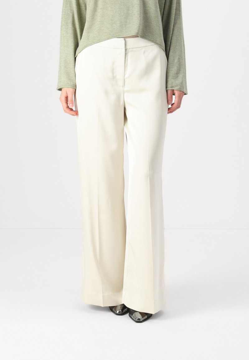 Wide-leg trousers in a light cream color, featuring a smooth fabric, clean front pleats, and a high waist design. Paired with a green top.