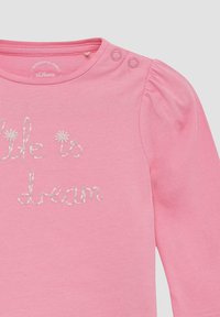 Rosa Langarm-Babykleidchen mit Puffärmeln, zwei Druckknöpfen an der Schulter und dem gestickten Schriftzug "Das Leben ist ein Traum" mit kleinen Blumendetails.