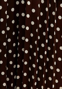Bruine stof met witte stippen, met een geplisseerd ontwerp. Het patroon bestaat uit gelijkmatig verdeelde, ronde stippen op een gladde textuur.