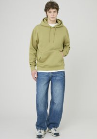 Sweat à capuche polaire vert olive avec poche avant et cordons, associé à un jean droit bleu clair et des baskets avec des accents multicolores.