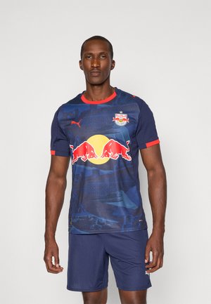 Mørkeblå Puma fodboldtrøje med røde detaljer, der har en stor gul cirkel og to røde okse-logoer. Korte ærmer, atletisk pasform.