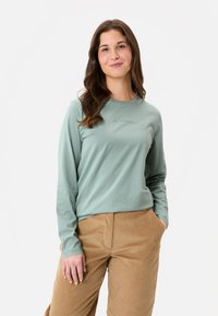 Langärmliges, hellgrünes Baumwollhemd mit Rundhalsausschnitt und dezenten Logodetails. Kombiniert mit hellen Cordhosen.