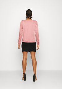 Blusa rosa a maniche lunghe con texture liscia che si abbina a una gonna nera aderente. Scarpe nere con tacco alto completano l'outfit.