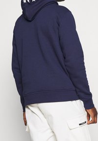 Sudadera azul marino con capucha, con tres estrellas blancas en la espalda, hecha de tela suave, con puños y bajo acanalados.