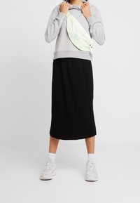 Sweat à capuche gris avec une poche kangourou, associé à une jupe mi-longue noire côtelée et des baskets blanches. Comprend un sac bandoulière vert clair avec une fermeture éclair.