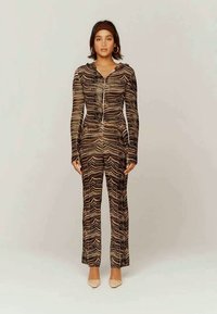 Zippered bodysuit in a brown and black wave pattern, featuring long sleeves and a fitted design, paired with light-colored shoes.