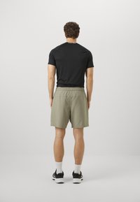 T-shirt atletico aderente nero e pantaloni corti verde oliva chiaro, realizzati in tessuto leggero, con vita elastica e dettaglio del logo sulla maglietta.
