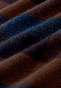 Miękka tkanina w odcieniach niebieskiego, brązowego i czarnego o teksturowanym, złożonym wyglądzie, podkreślająca przytulny, tkany wzór.