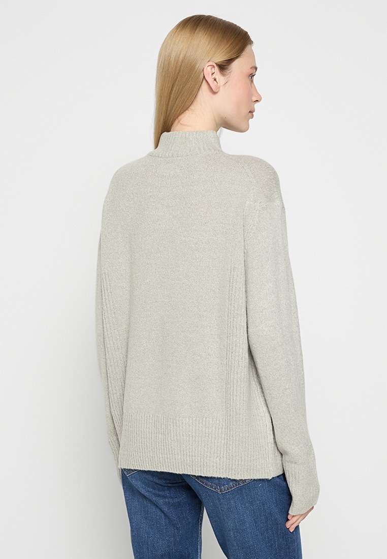 Maglione pullover grigio chiaro con colletto alto, polsini a coste e dettagli nei pannelli laterali. Tessuto morbido, vestibilità rilassata e schiena leggermente più lunga.