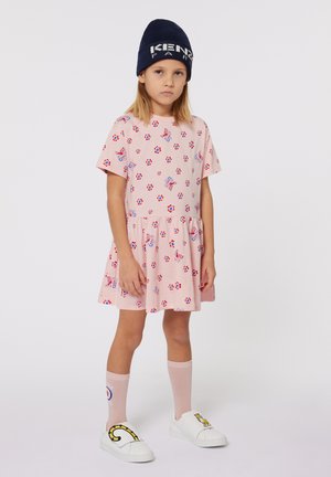 Lichtroze jurk met korte mouwen, bloemmotief en geplooide rok. Draag het met witte instap-schoenen en roze kniekousen. Marineblauwe beanie.