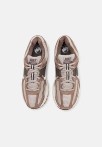 Nike Vomero 5 αθλητικά παπούτσια με συνδυασμό καφέ δικτυωτού υφάσματος και σουέτ, λευκές λεπτομέρειες, παχιά αφρώδη σόλα και γκρι κορδόνια.