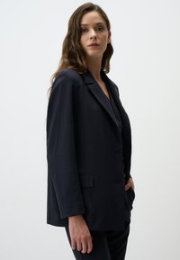 Blazer a righe navy, design monopetto, rever a punta, tessuto testurizzato, tasche frontali, vestibilità rilassata, stile minimalista.