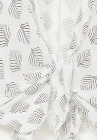 Biała tkanina z teksturowanym splotem i czarnymi wzorami liści, z postrzępionymi brzegami i drapowaną konstrukcją w centrum.