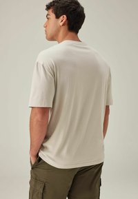 Tricou din bumbac bej, cu guler rotund, mâneci scurte și un croi lejer, asortat cu pantaloni scurți cargo verzi închisi.