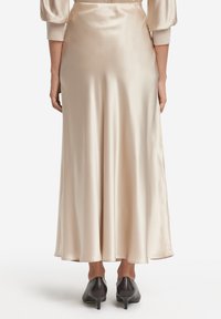 Satin midikjol i ljusbeige, med en flödande design, mjuk textur och en subtil lyster, matchad med spetsiga svarta klackar.