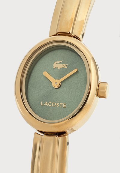 Златен ръчен часовник със зелен циферблат, златни стрелки, лого Lacoste и емблема на крокодил върху метална верижка.