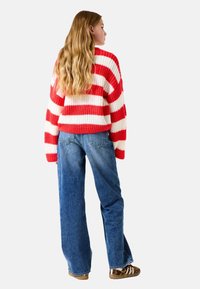 Rot-weißer gestreifter Strickpullover mit lockerer Passform, kombiniert mit hellblauen weiten Jeans und braunen Sneakers.