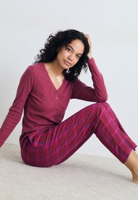 Dyp burgunder langermet henley-genser med knapper, kombinert med rutete burgunder- og rosa pysjbukser, med en avslappet passform og myk tekstur.