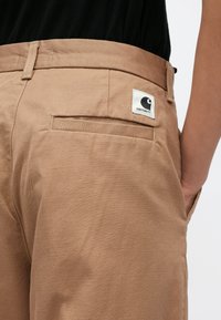 Καφ�έ βαμβακερό παντελόνι με ομαλή υφή, που διαθέτει πίσω τσέπη και ετικέτα με το λογότυπο Carhartt στη μέση.
