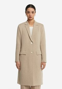 Beige Wollmantel mit langen Ärmeln, Reverskragen und zwei vorderen Taschen. Verfügt über zwei große Knöpfe und eine gerade Silhouette.