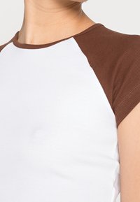 Kortärmad skjorta med vit kropp och bruna raglanärmar, ribbad textur, rund halsringning och figurnära design.