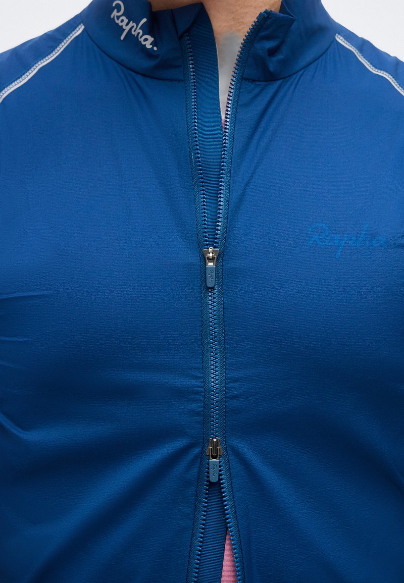 Close-up of a blue Rapha cycling jersey with dual zippers partially zipped and the Rapha logo visible on collar and chest.