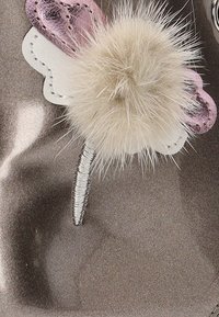 Accesorio de mariposa colorido con alas metálicas de color púrpura y blanco, un centro de pom-pom beige esponjoso y un tallo de alambre plateado.