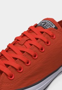 Κόκκινο sneaker χαμηλού τύπου με κόκκινες κορδόνια που ταιριάζουν, κόκκινα παπούτσια και λευκή καουτσούκ σόλα με μαύρη ρίγα, με λογότυπο Converse σε ραμμένη ετικέτα.