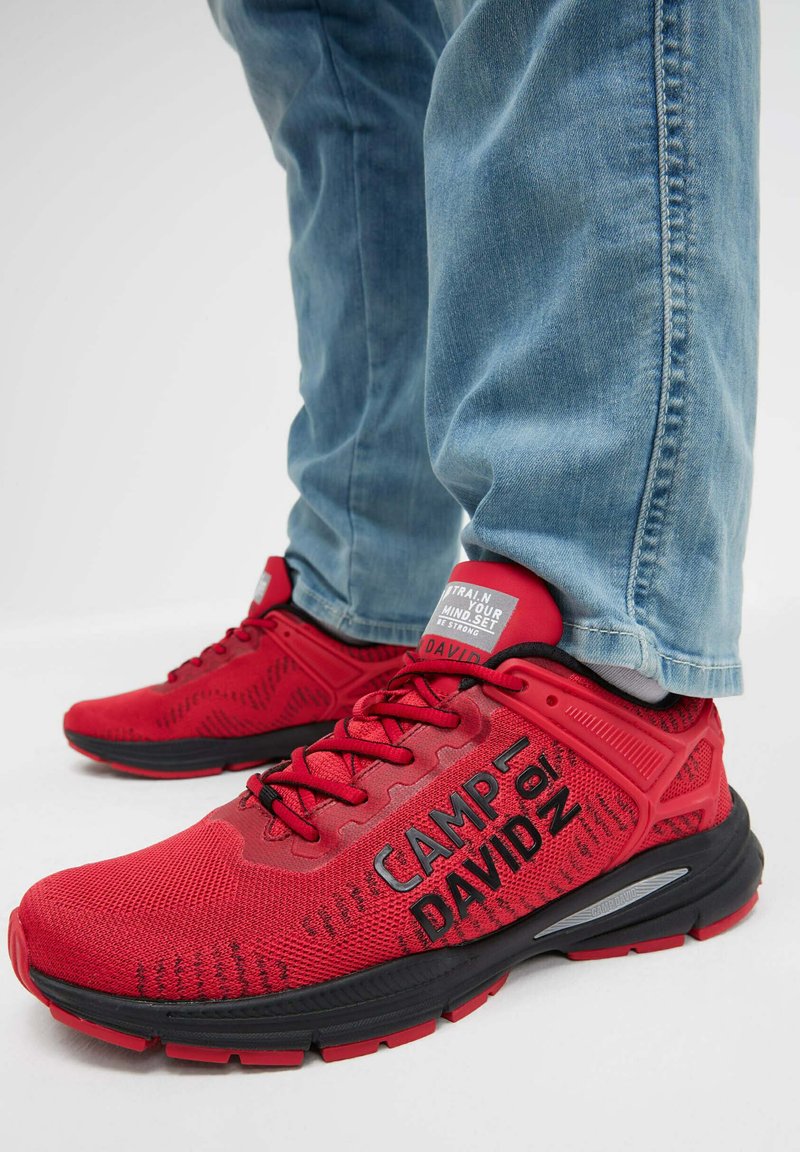 Rote Sportschuhe mit einem strukturierten Mesh-Obermaterial, schwarzen Akzenten und "CAMP of DAVID" Branding. Kombination mit hellblauen Jeans.