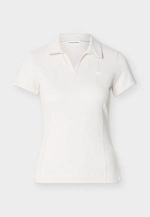 Λευκό πόλο πουκάμισο με υφασμένο μοτίβο, κοντά μανίκια και V-λαιμόκοψη. Διαθέτει μικρό λογότυπο στο αριστερό μέρος του στήθους.