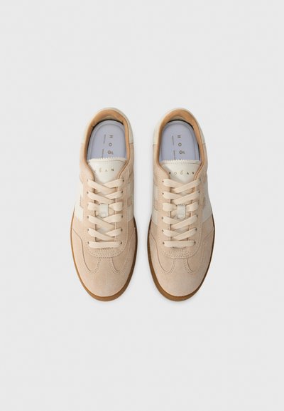 Een paar beige suède sneakers met witte strepen en veters, vanuit bovenaf gezien op een effen witte achtergrond.