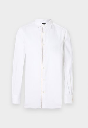 Fehér hosszú ujjú ing, begombolva, klasszikus gallérral. Sötét nadrággal és fényes fekete cipővel viselve. Sima anyag, szabott fazon.